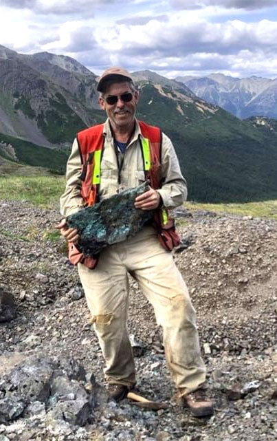 David Moore stands on a mountain slope, holding a briefcase-sized chunk of green rock.