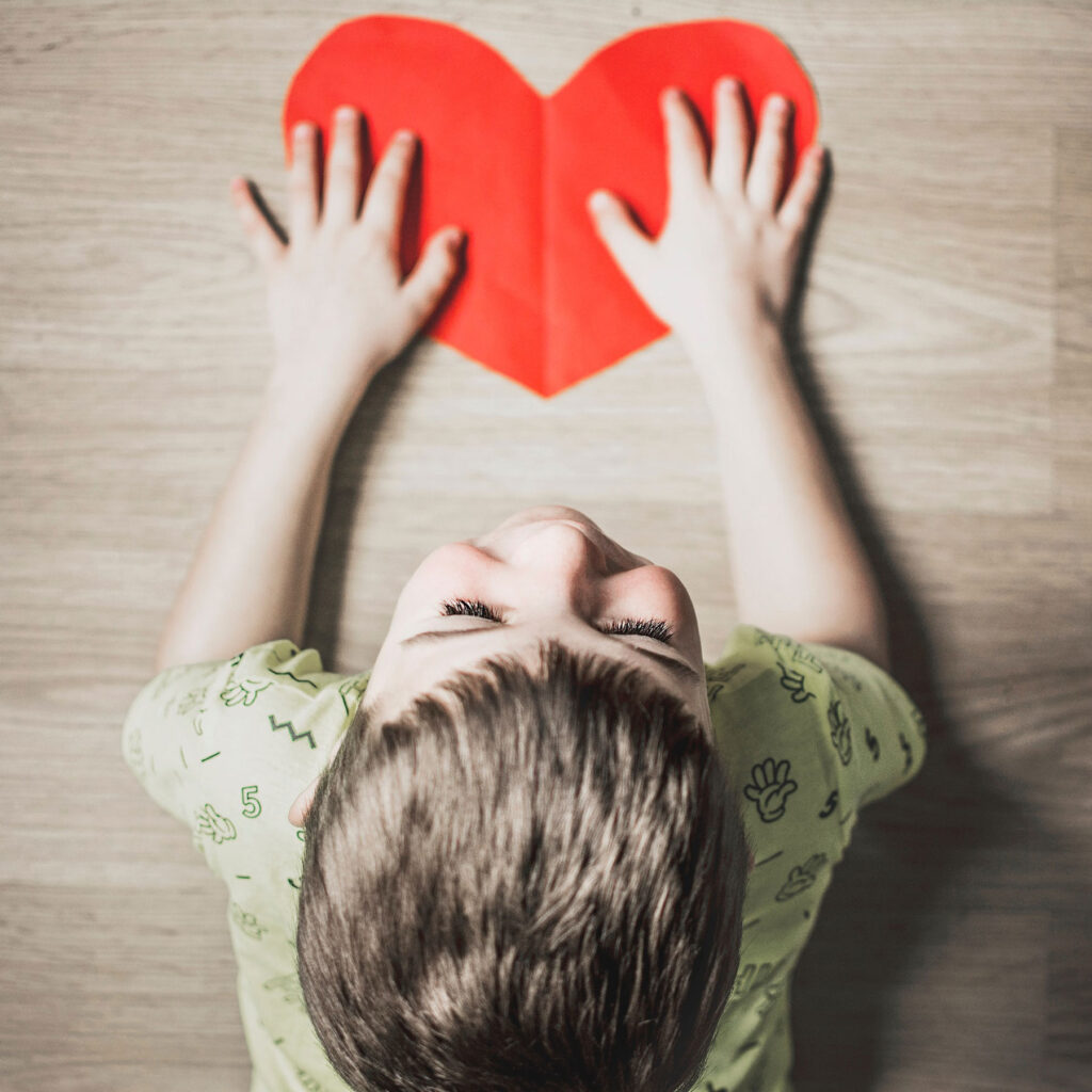 A young boy smiles as he lays out a big paper heart on a table.