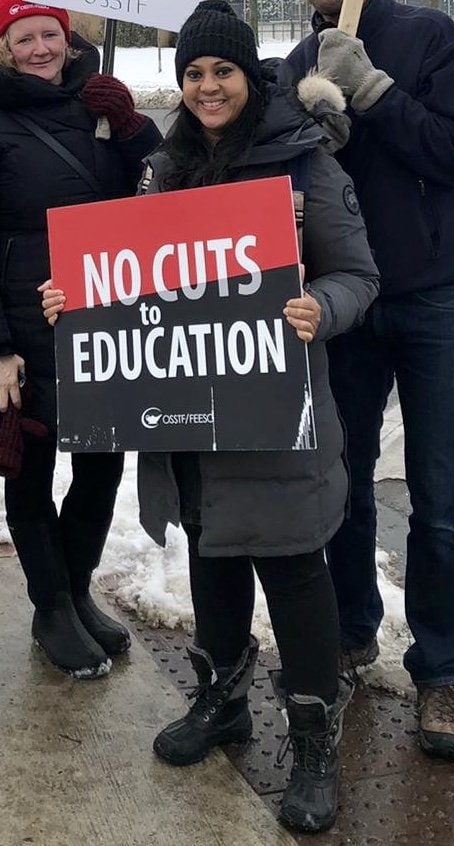 Fariah Chowdhury, dressed for winter weather, holds a sign that reads: No cuts to education.