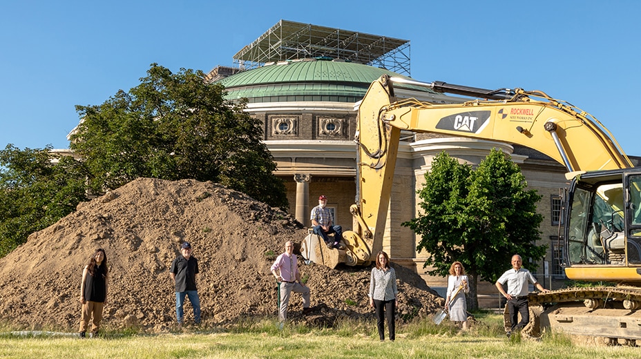 President Meric Gertler and other U of T executives sit and stand on a parked backhoe and enormous pile of earth.