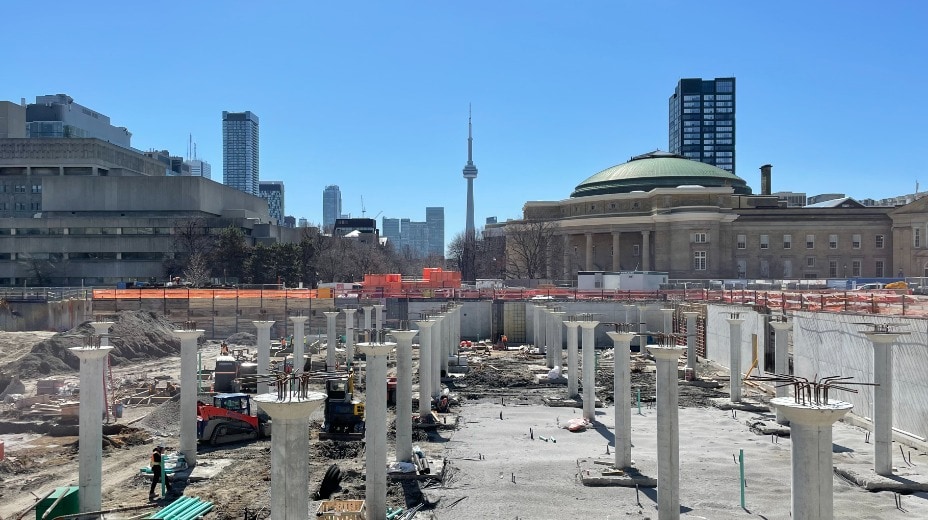 A forest of concrete pillars rise up out of a construction site. Convocation Hall can be seen in the background.