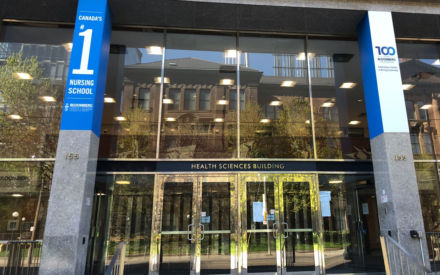 A street scene reflected in sparkling windows of the Bloomberg School of Nursing. Poster reads: Canada's #1 nursing school.