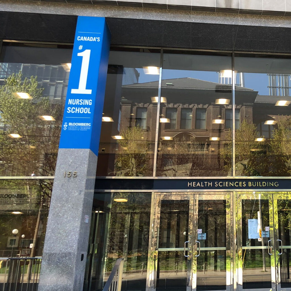 A street scene reflected in sparkling windows of the Bloomberg School of Nursing. Poster reads: Canada's #1 nursing school.