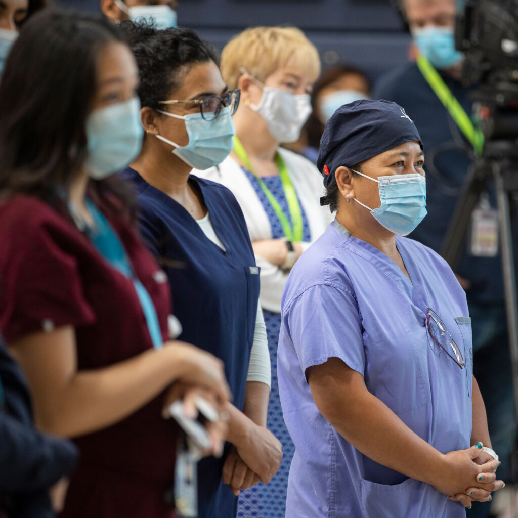 People wearing masks, some of them in health-care scrubs, stand together looking serious.