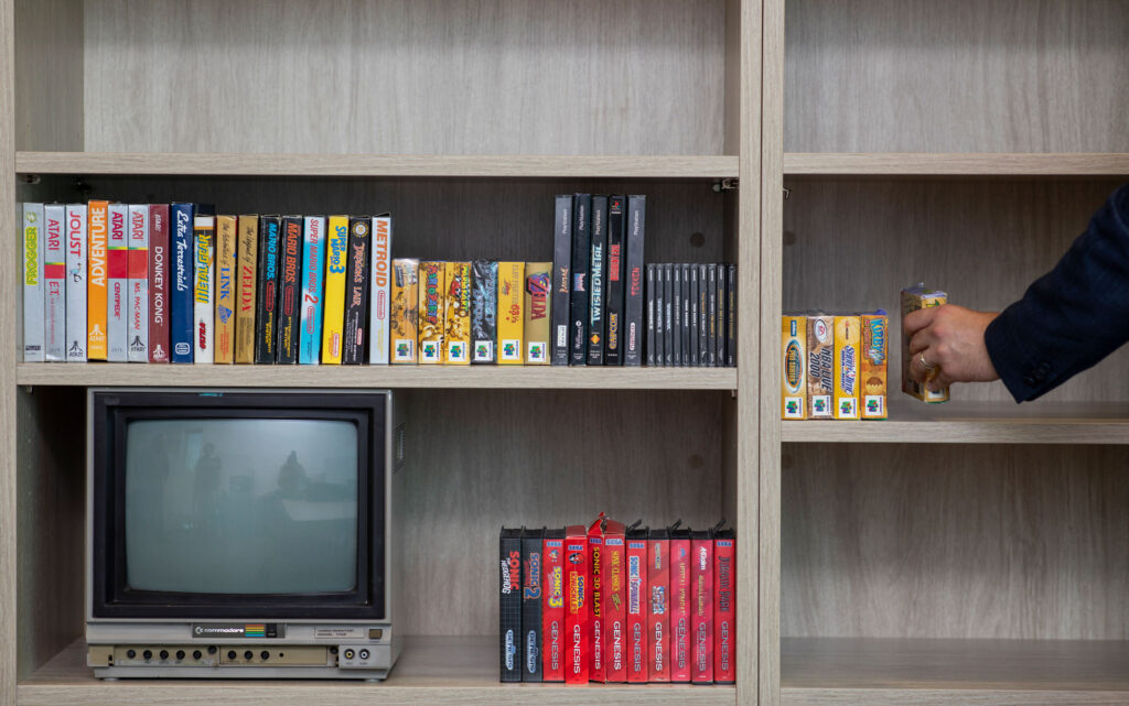 A bookshelf holding differently sized video games and an old-fashioned TV.