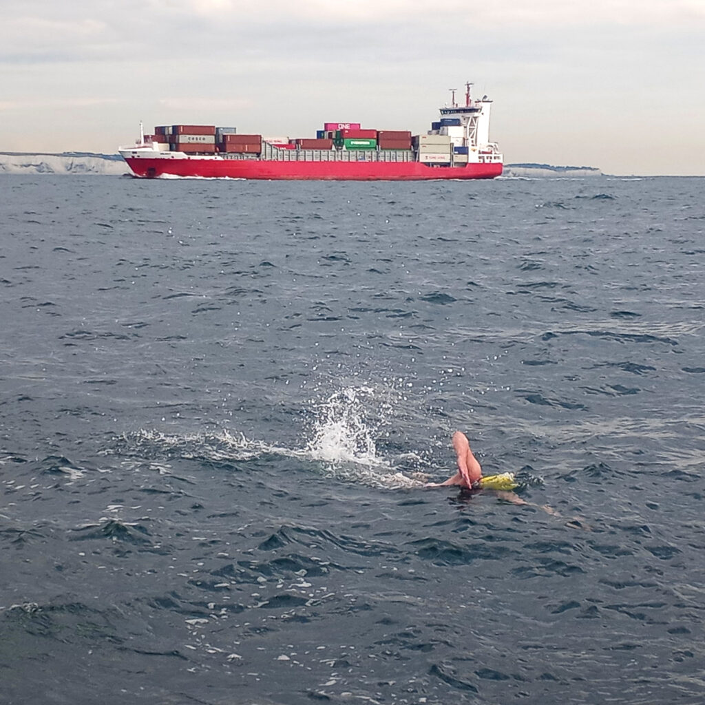 Sean Nuttall swims in choppy water in front of a container ship and the white cliffs of Dover.