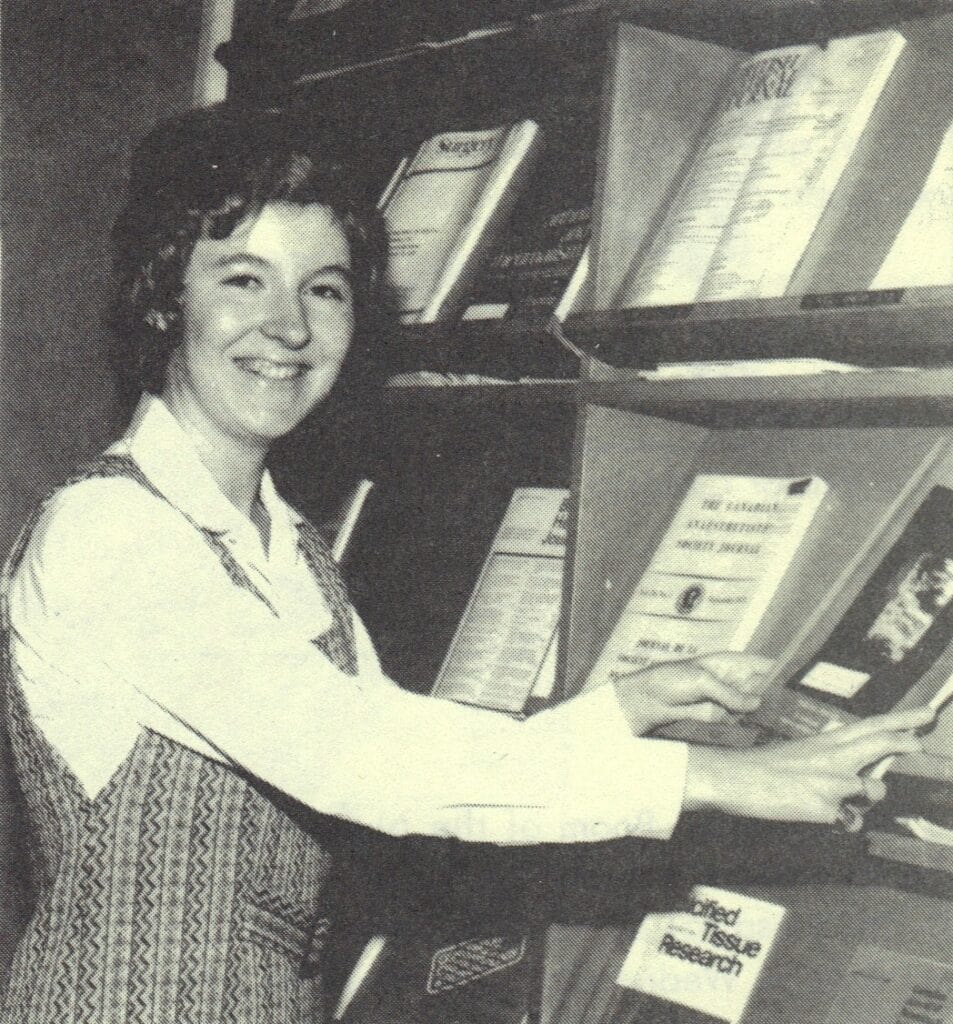 In a photo from 1974, Elizabeth Reid smiles as she arranges medical journals on a display shelf.