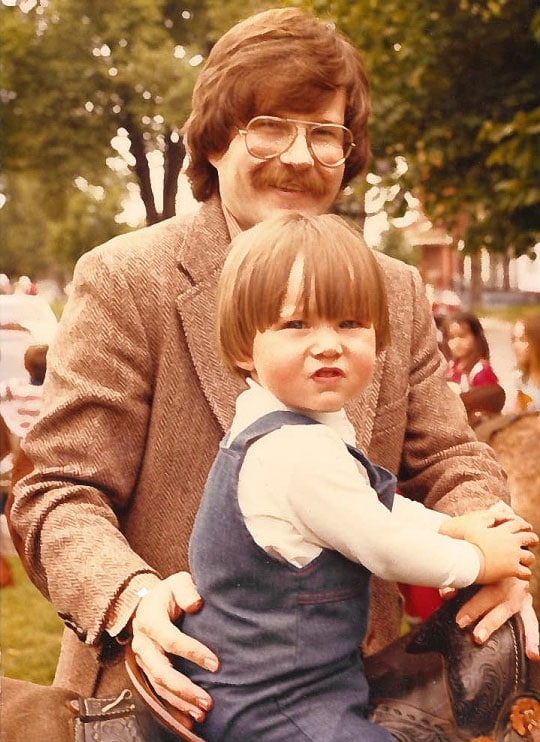 In a photo from the 70s, Robert Nuttall holds his toddler son Sean on a ride in a park.