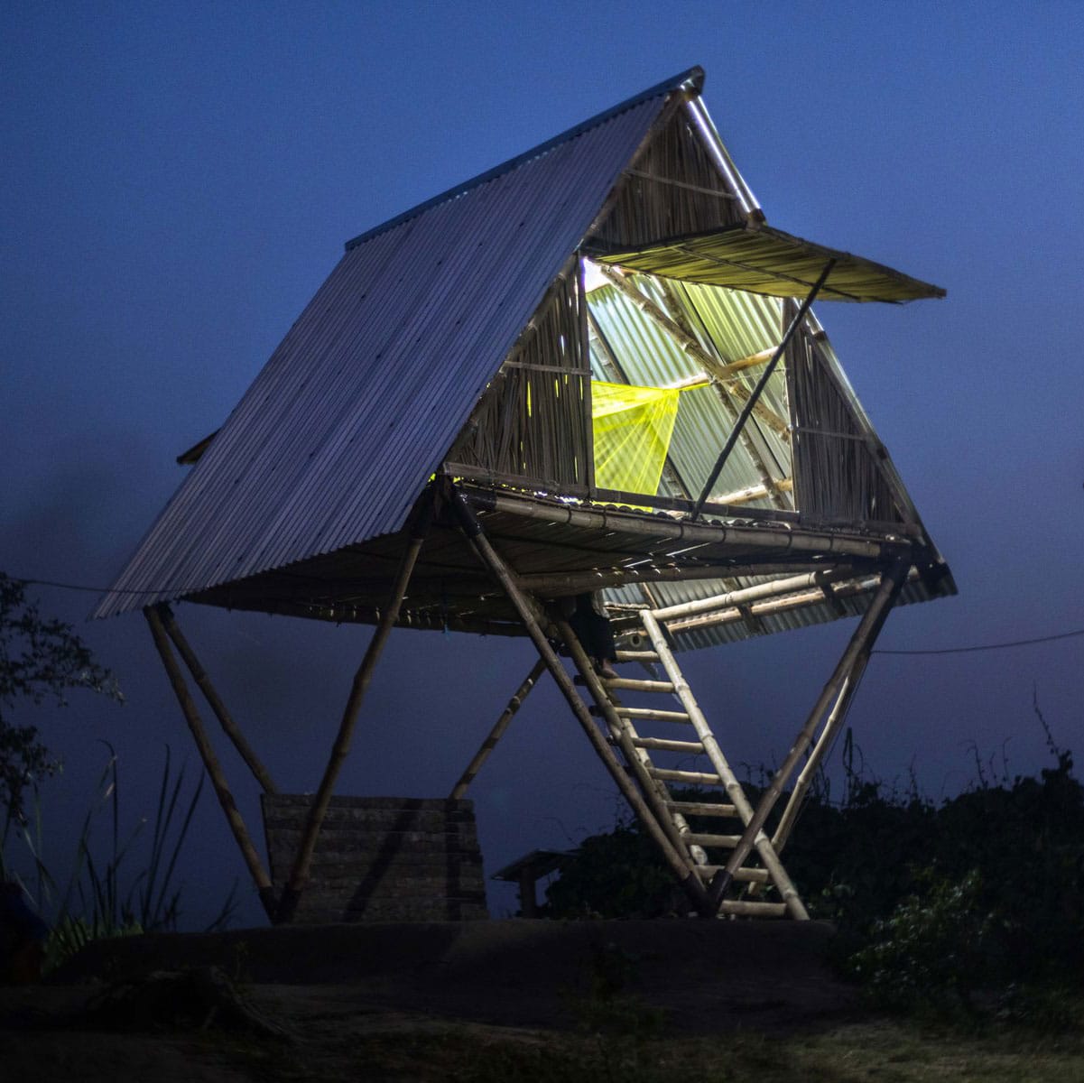 A triangular building on stilts is made from wood, reeds, and corrugated iron.
