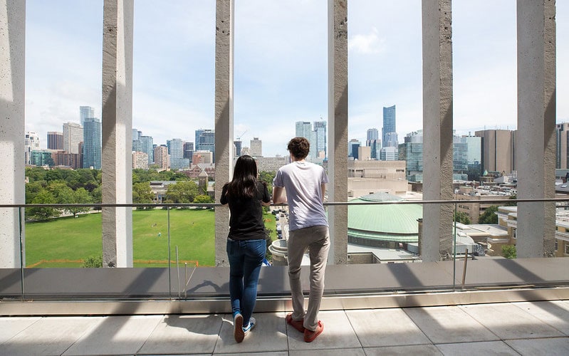 Two students lean on a railing on the balcony at U of T Engineering, looking over Front Campus.