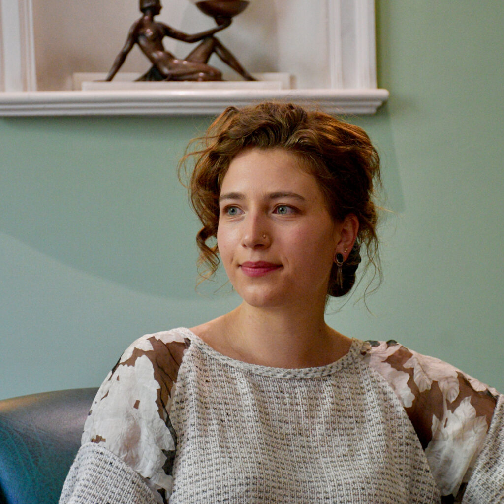 Karine Hack smiling as she sits on a sofa by a statue of a woman holding a lamp.