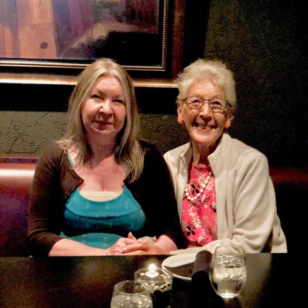 Tracy Barber and Marjorie Sorrell smile together, sitting in a restaurant booth.