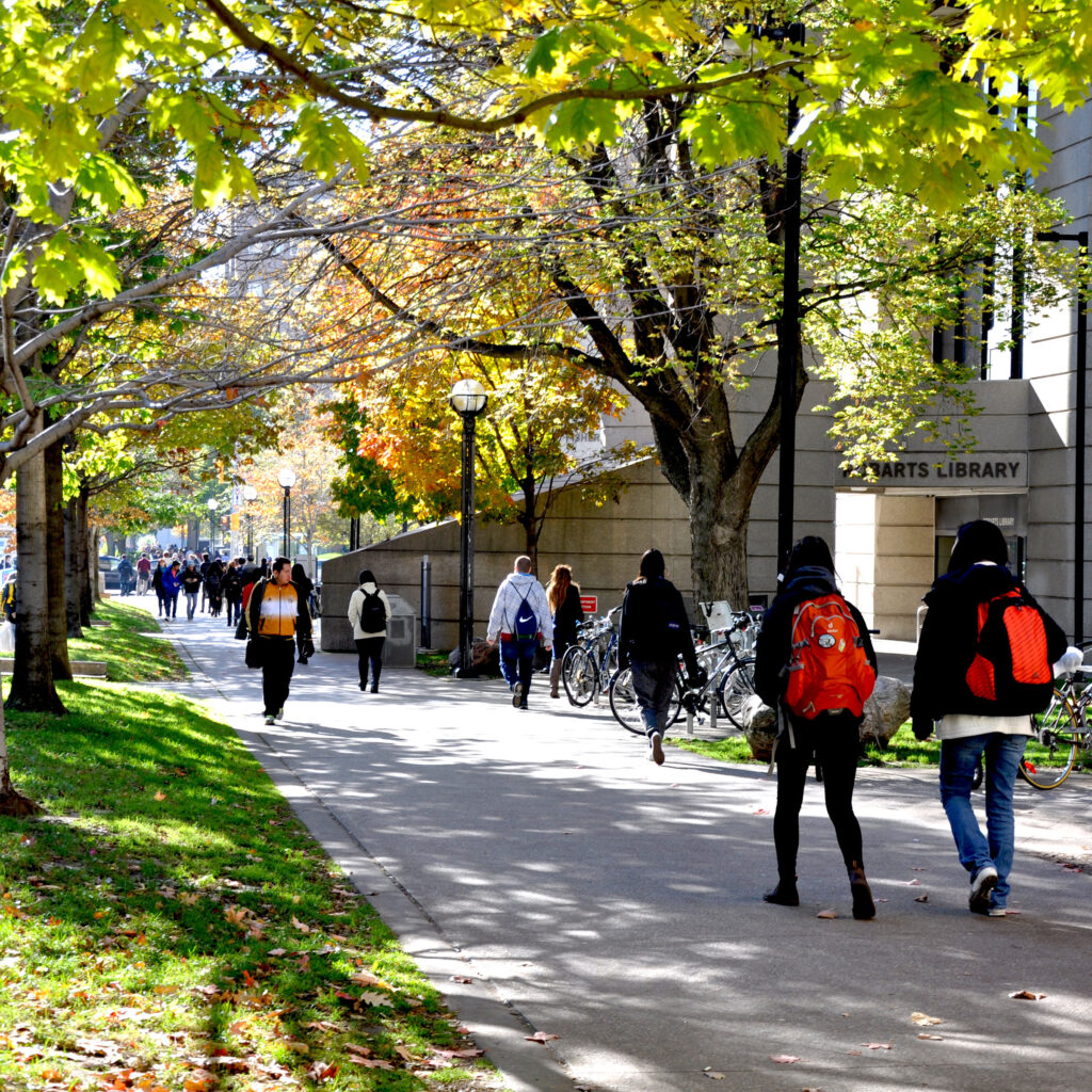 Students walk under the trees outside Robarts library on a sunny autumn day.
