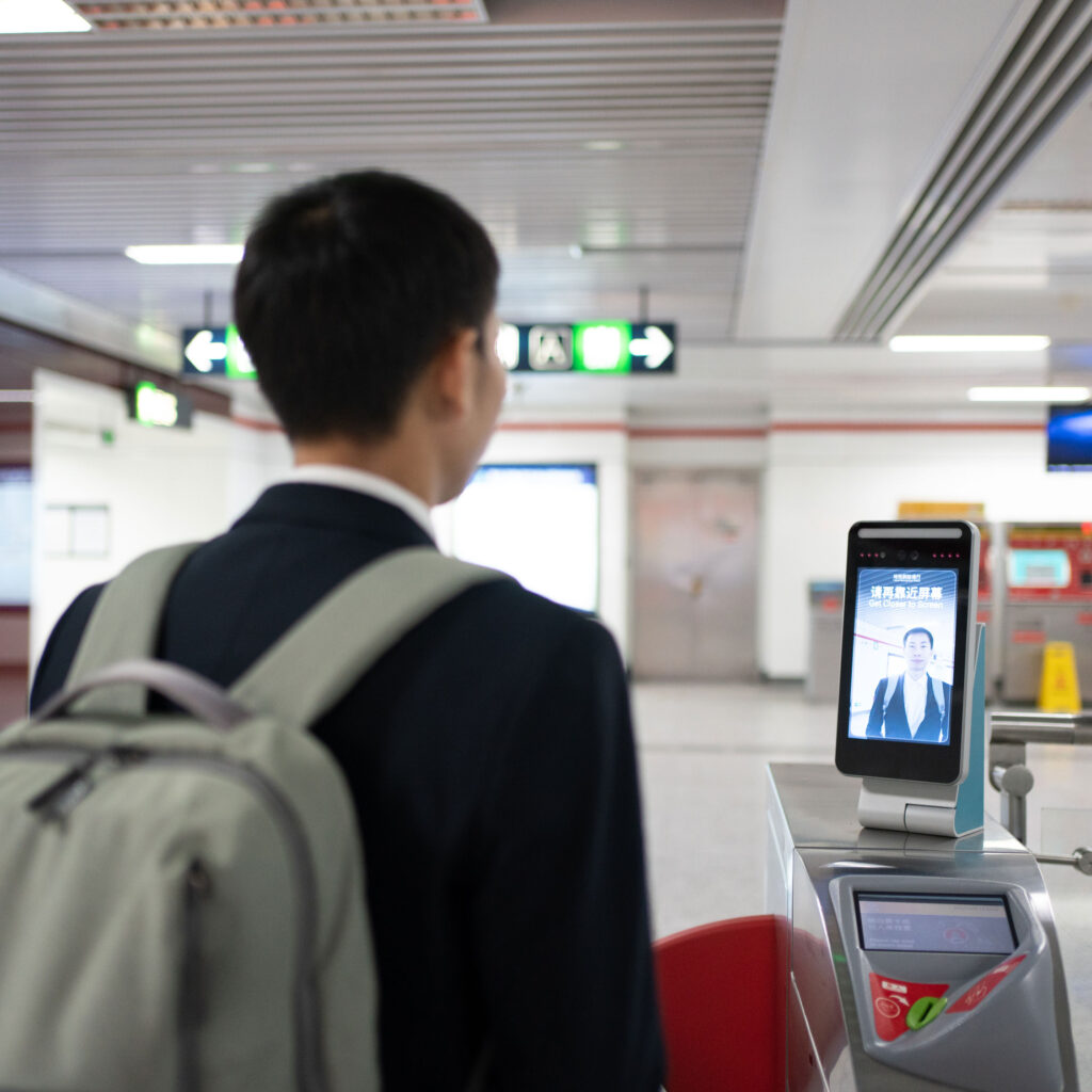 An Asian man in a suit lets a screen on an airport turnstile scan his face.