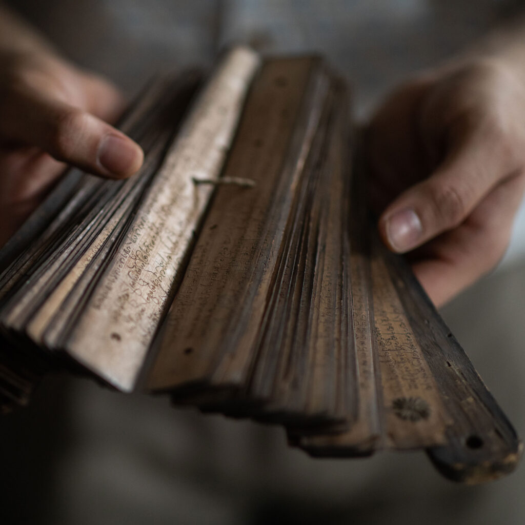 Flat wooden strips, looking very old, are joined with string through a central hole, and covered in an elaborate script.