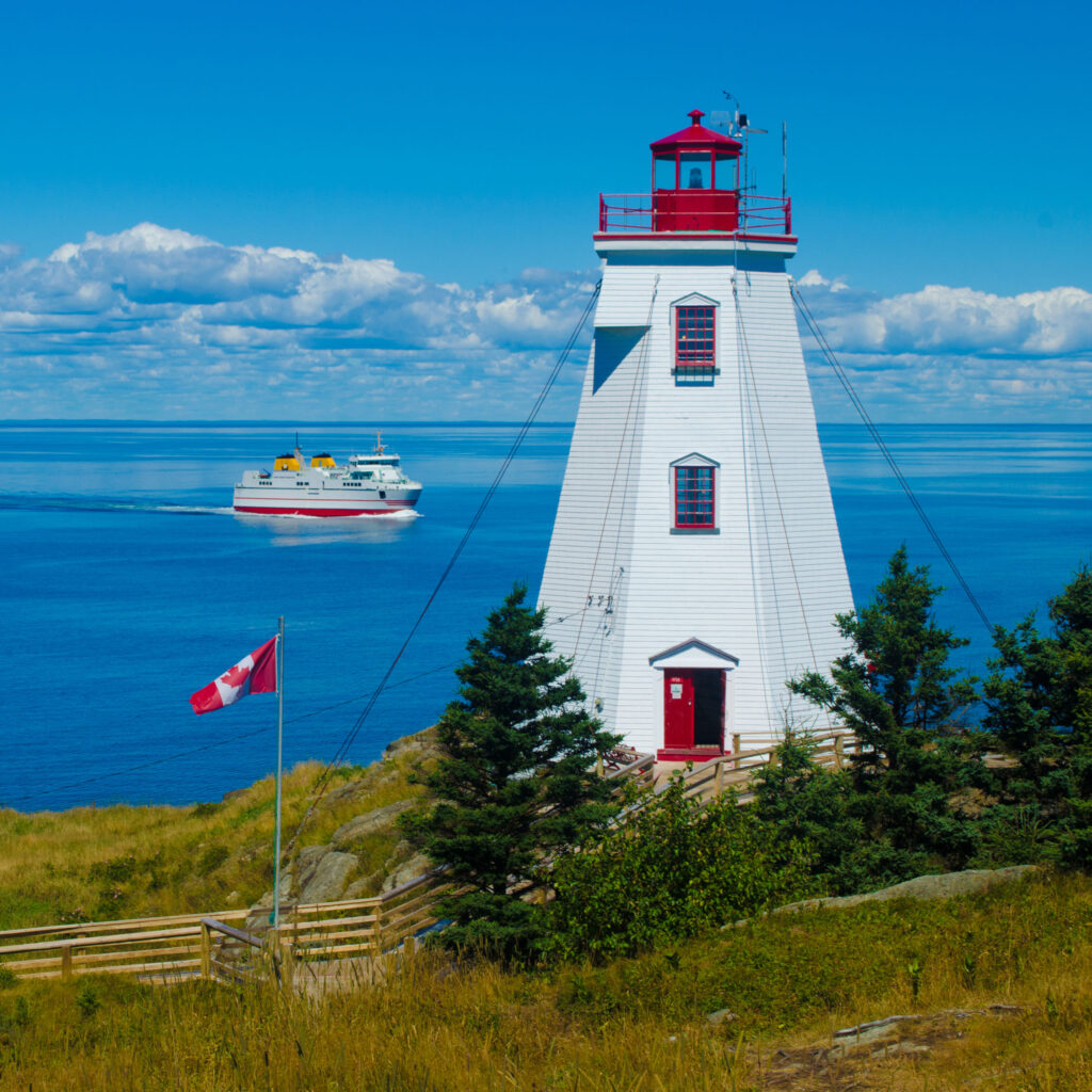 On a sunny day, an old wooden lighthouse on Grand Manan Island stands facing a calm sea.