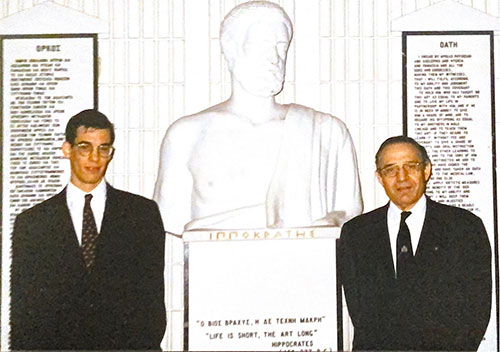 George and Dimitrios Oreopoulos stand with a marble bust of Hippocrates. Text: Life is short, the art long.