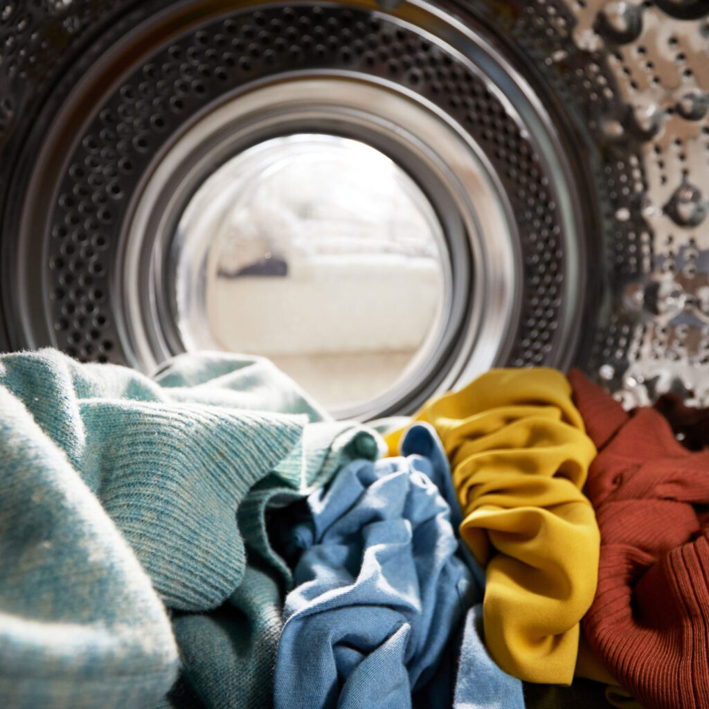 Colourful clothes piled inside a washing machine in a laundromat.