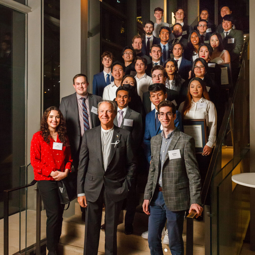 Pierre Lassonde smiles as he poses with 29 of the Lassonde Scholars on a staircase.