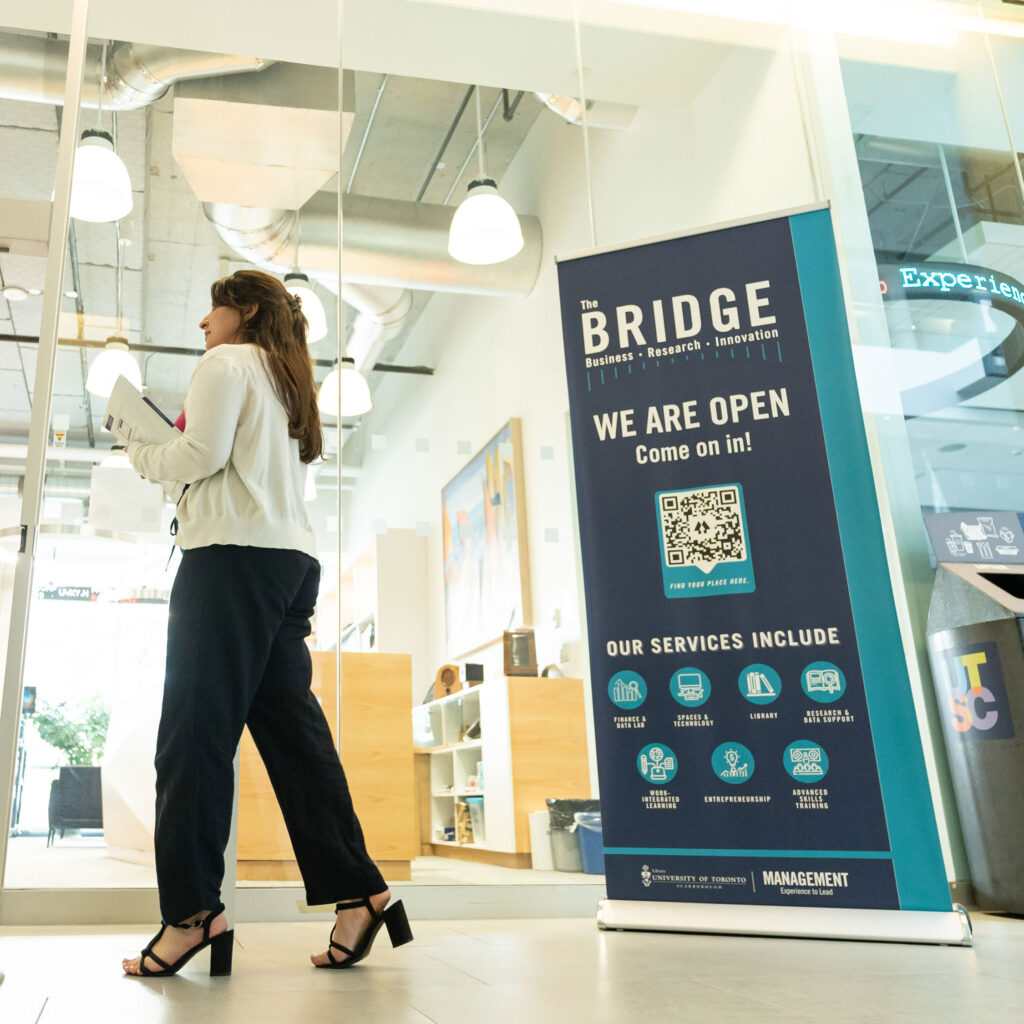 A woman walks by a sign that reads: The Bridge, business, research, innovation.