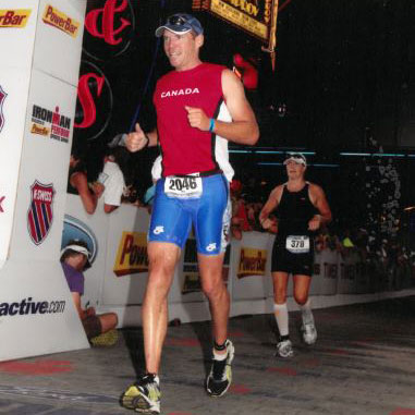 Mike Walker smiles as he jogs across a race finish line at night.