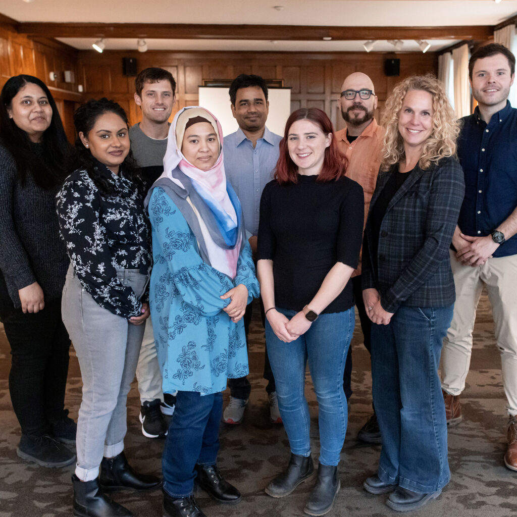 Several students and professors pose for a picture in a wood-panelled room.