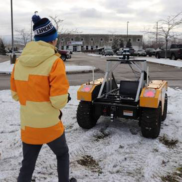 James Xu walking behind an unmanned four-wheel vehicle in a snowy parking lot.