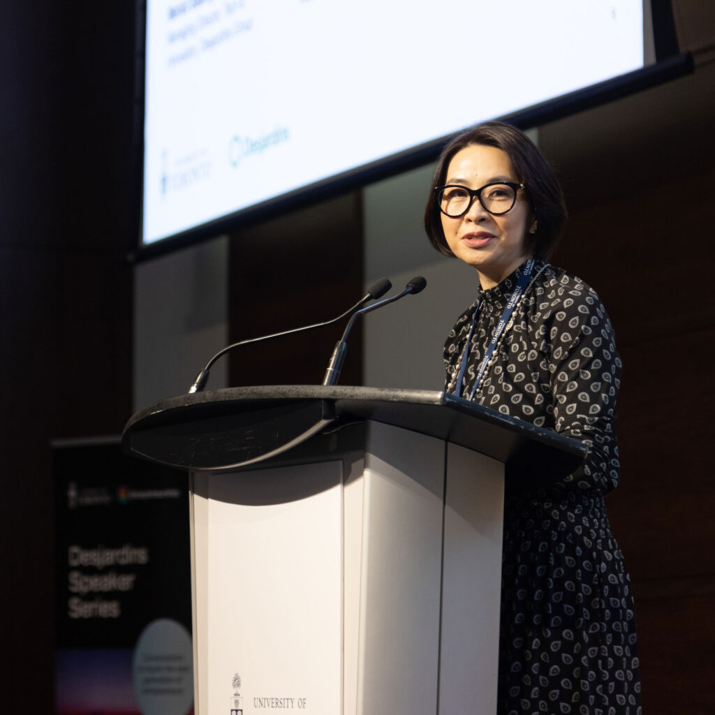 Eva Lau smiles as she speaks at a podium on stage.