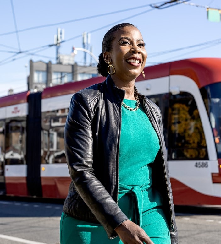 Angela Gibson smiling and walking past a Toronto streetcar on a sunny day.