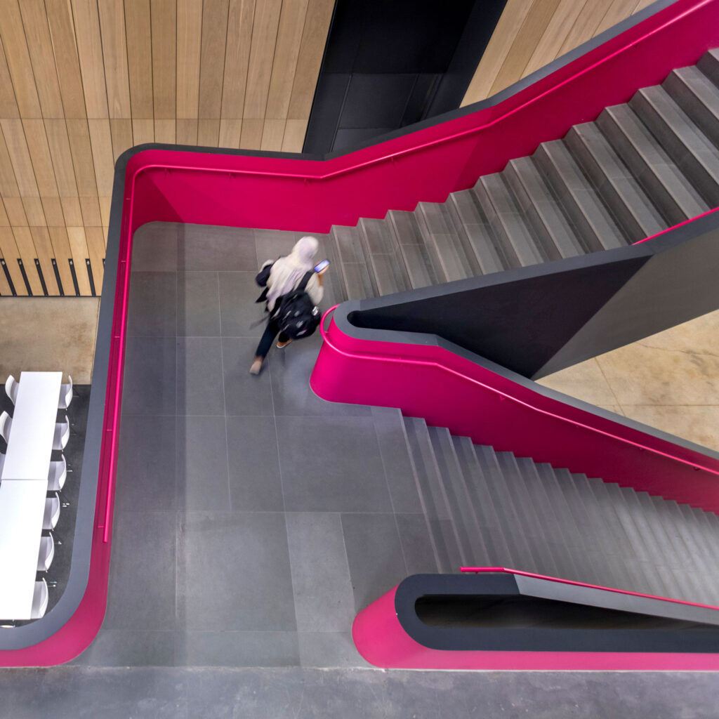 A woman carrying a backpack walks up the pink staircase at the Rotman School