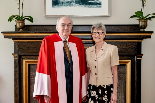 Michael and Virginia Walsh at convocation, smiling in front of mantel.