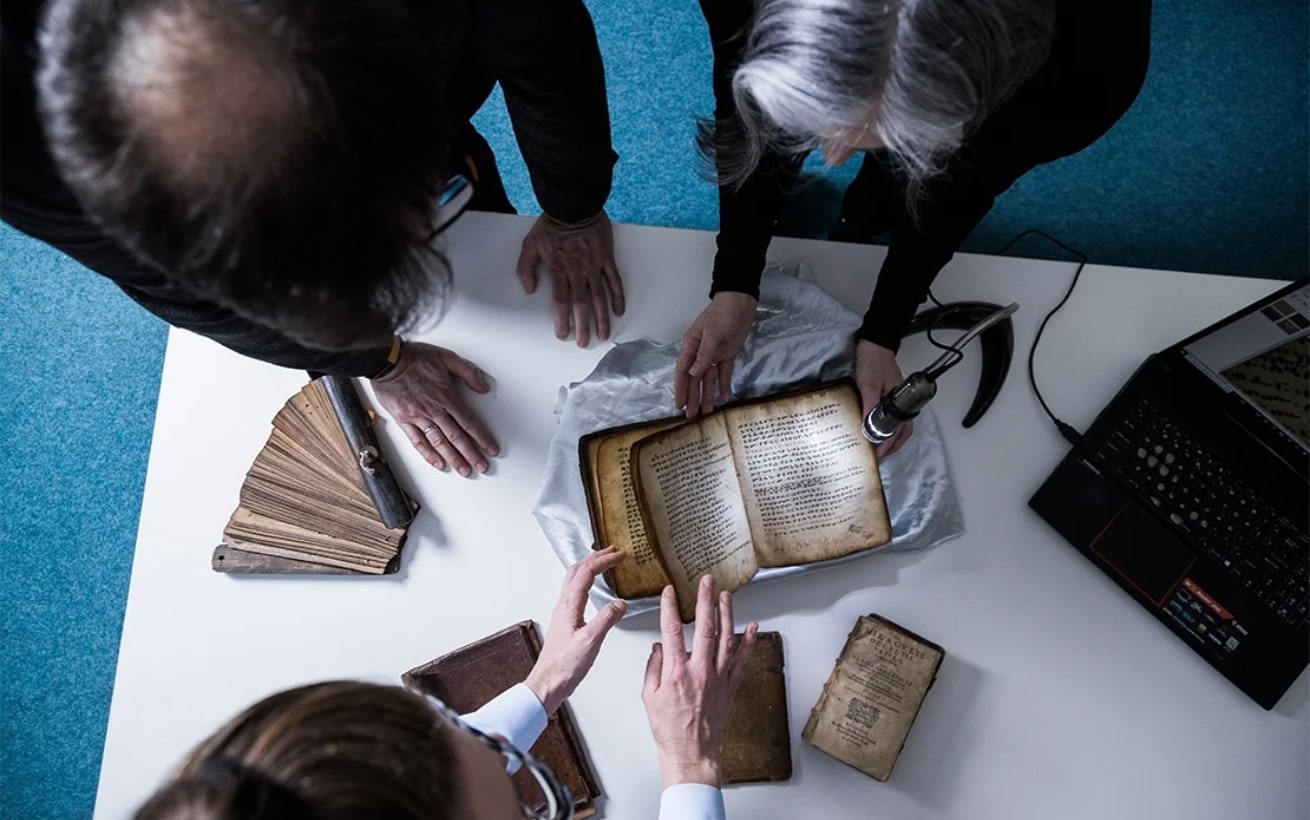 An overhead view of three people inspecting old books at a table