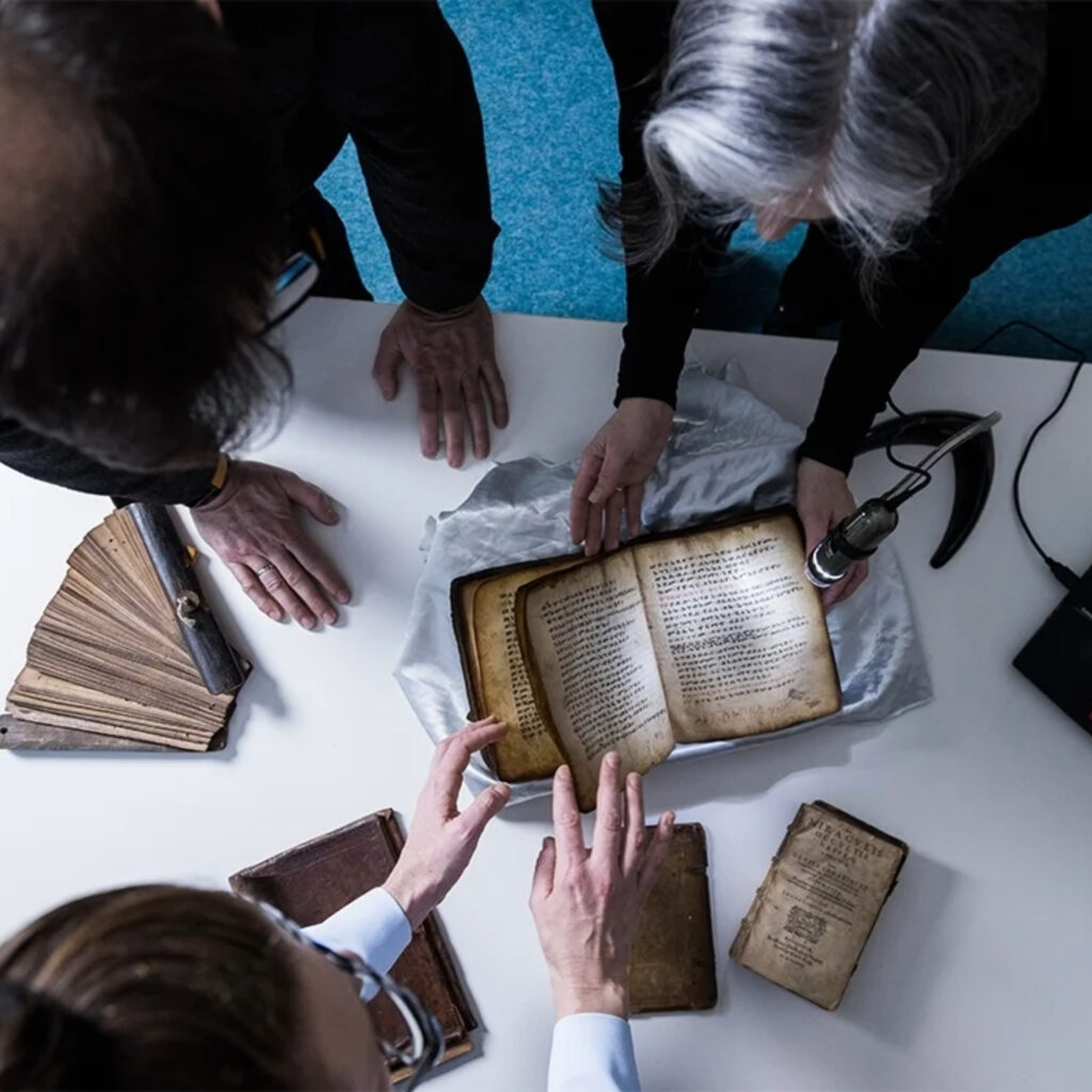 An overhead view of three people inspecting old books at a table