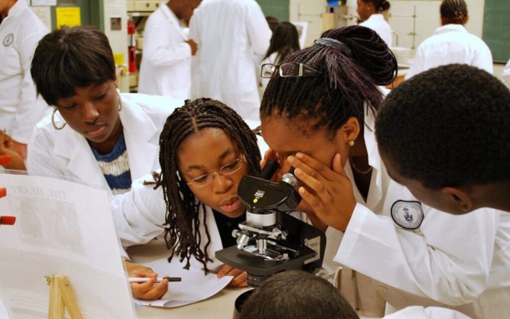 Students wearing lab coats looking through a microscope