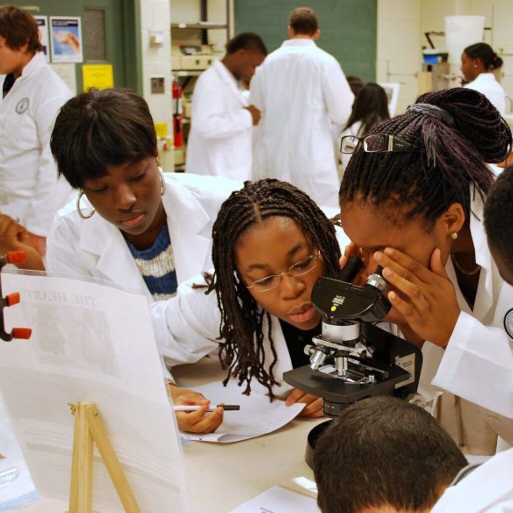 Summer students in lab coats looking through a microscope