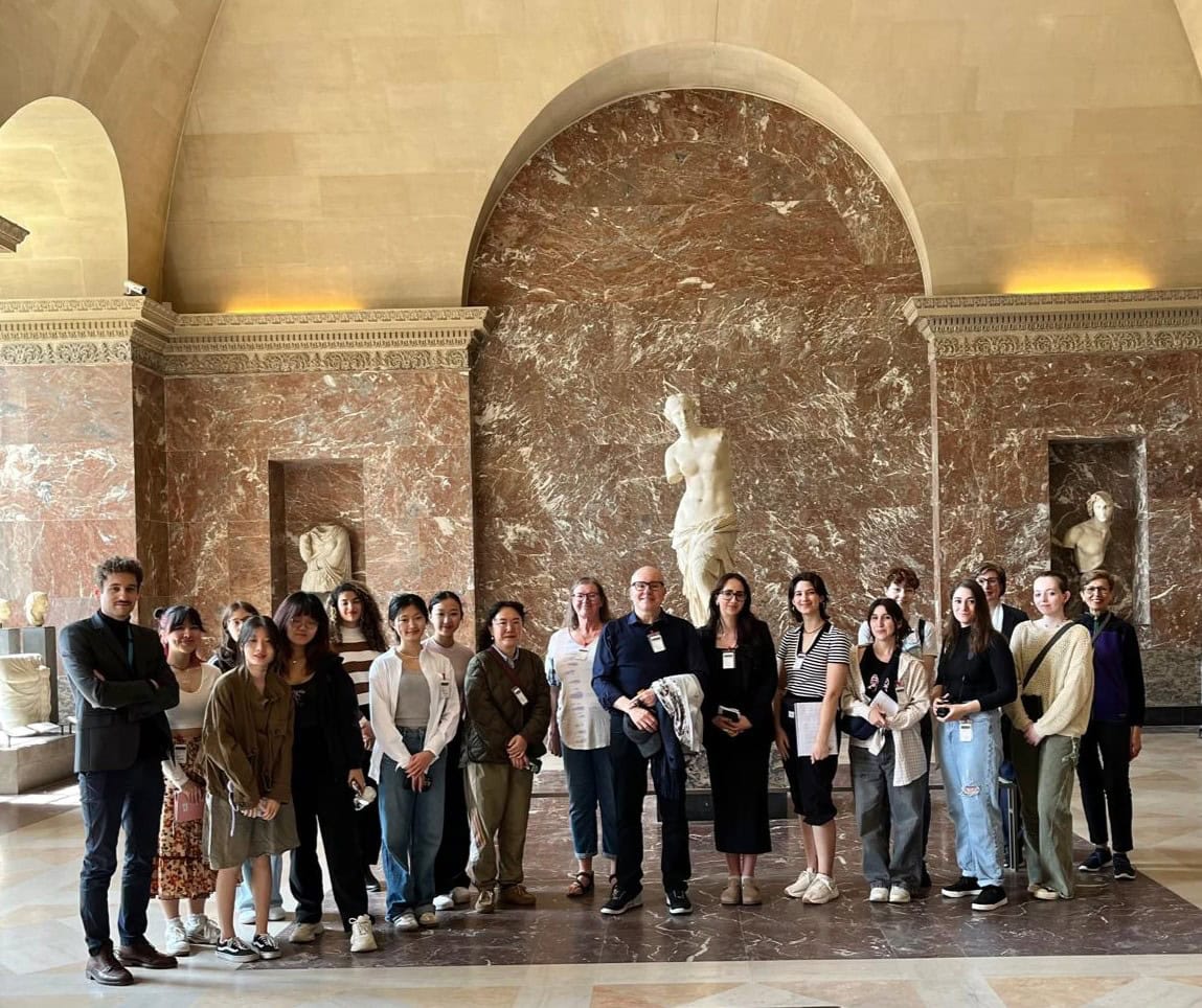 A group of students poses in front of the Venus de Milo statue at the Louvre Museum.