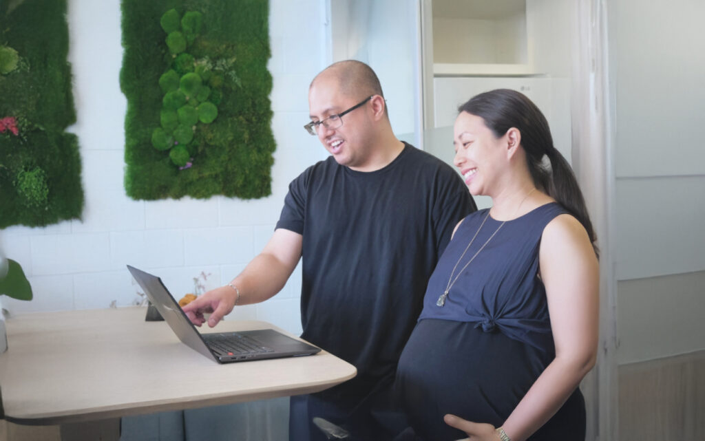 A pregnant person and another person standing by a laptop