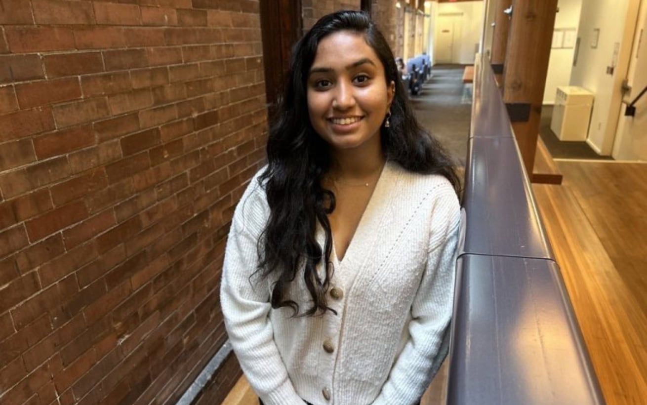 A woman standing and smiling in a hallway.