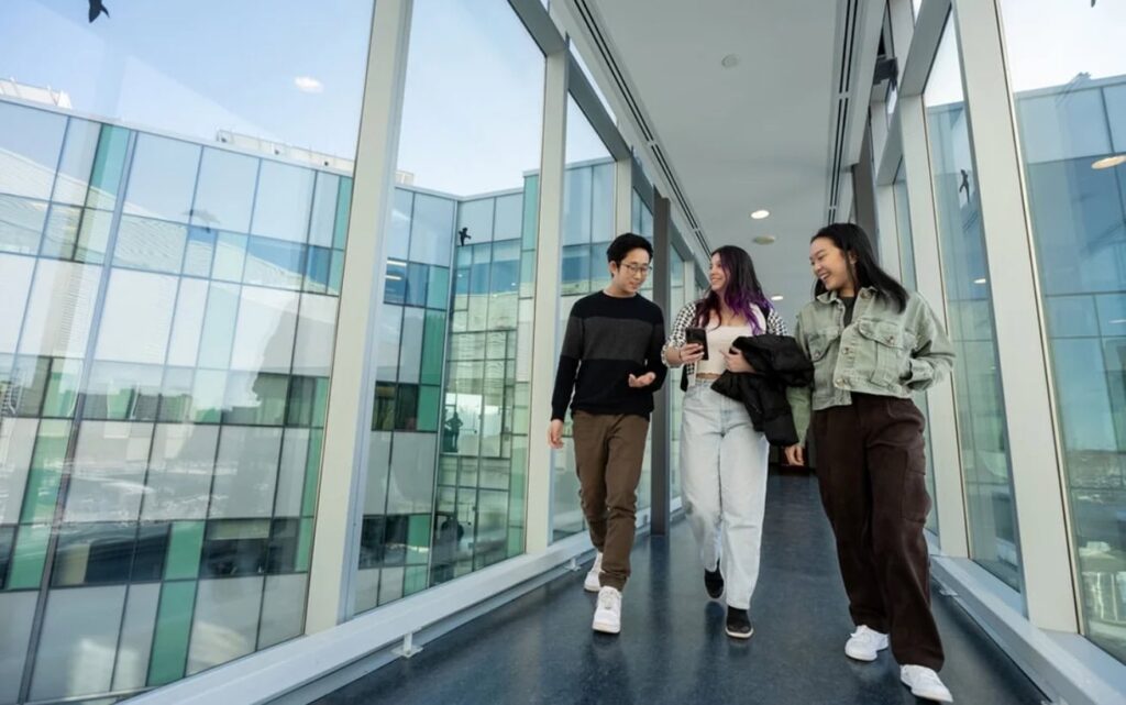 Three students walking together down an elevated indoor walkway.