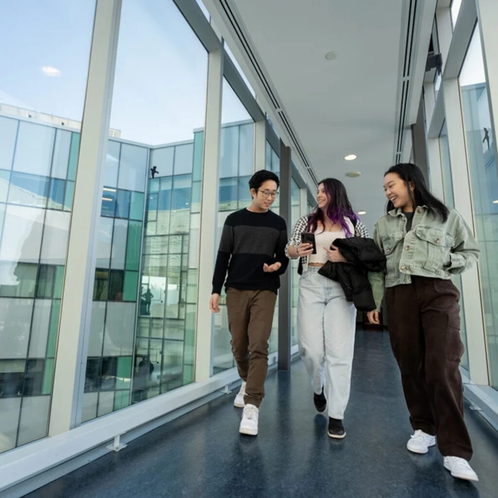 Three students walking together down an elevated indoor walkway. 