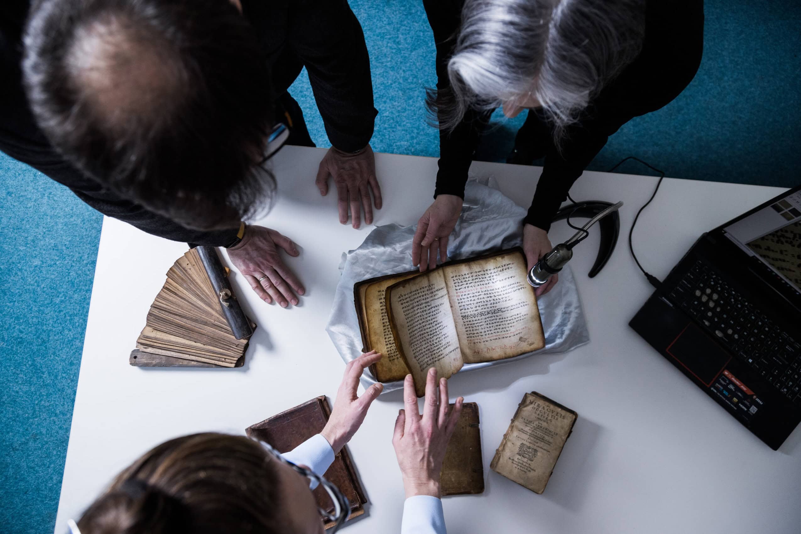 An overhead shot of three people looking at old books