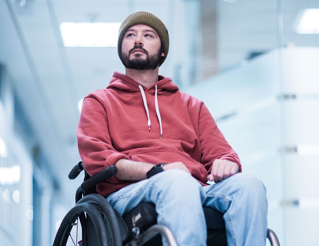 Image of Beau Hayward sitting in his wheel chair, wearing a red sweater, light blue jeans, and green toque.