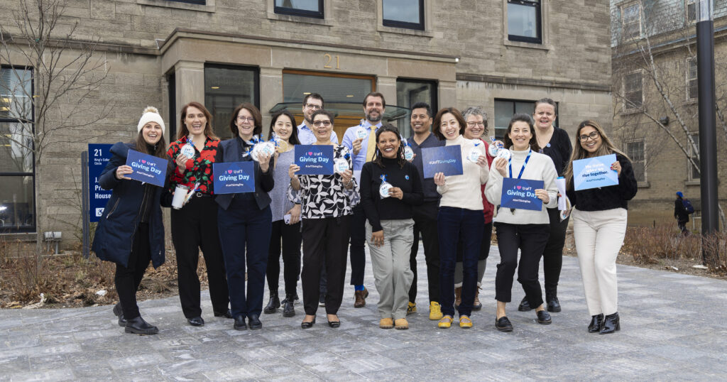 U of T staff gathered outside King's College, holding blue and white Giving Day signs in a group photo