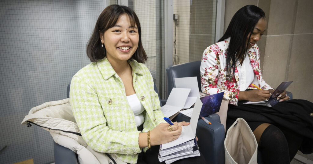 Two UofT Giving Day ambassadors (Rachel Ma and Janielle Browne), seated in Sid Smith lobby, writing Thank You cards to donors
