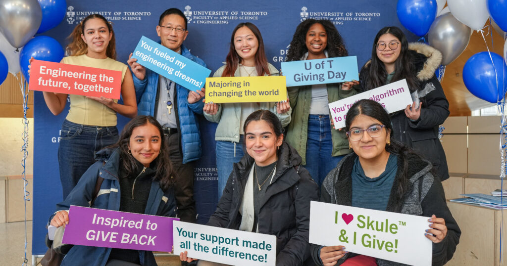 Dean of Engineering, Chris Yip, joins smiling Engineering students in a group portrait, holding Giving Day signage and photobooth props