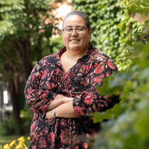 A person wearing a printed dress standing in front of some greenery