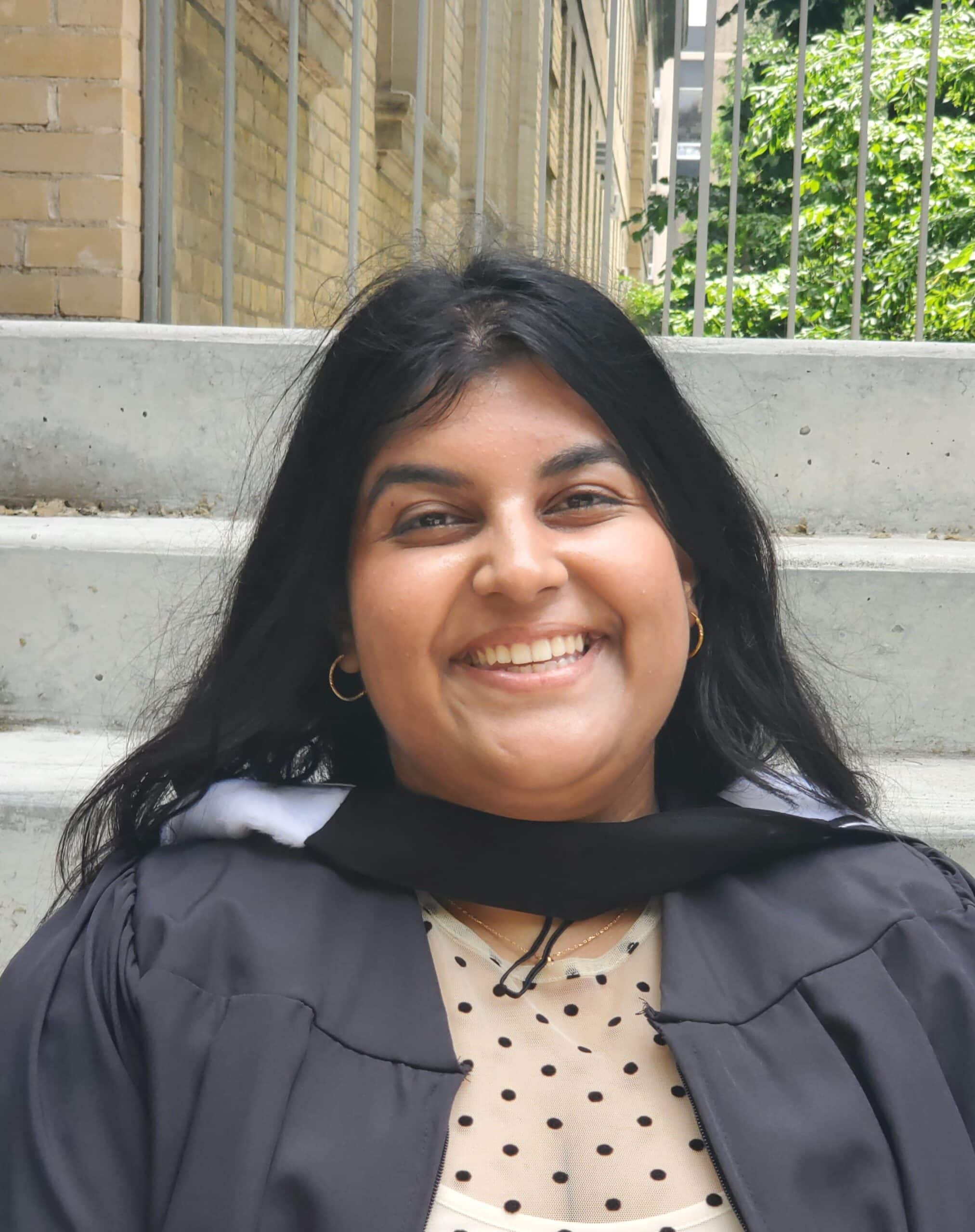 A woman with a big smile wearing her graduation gown.