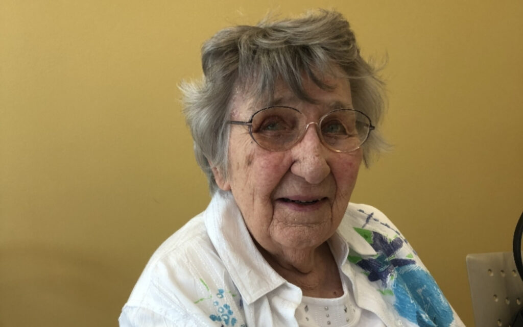 An elderly woman seated and smiling.