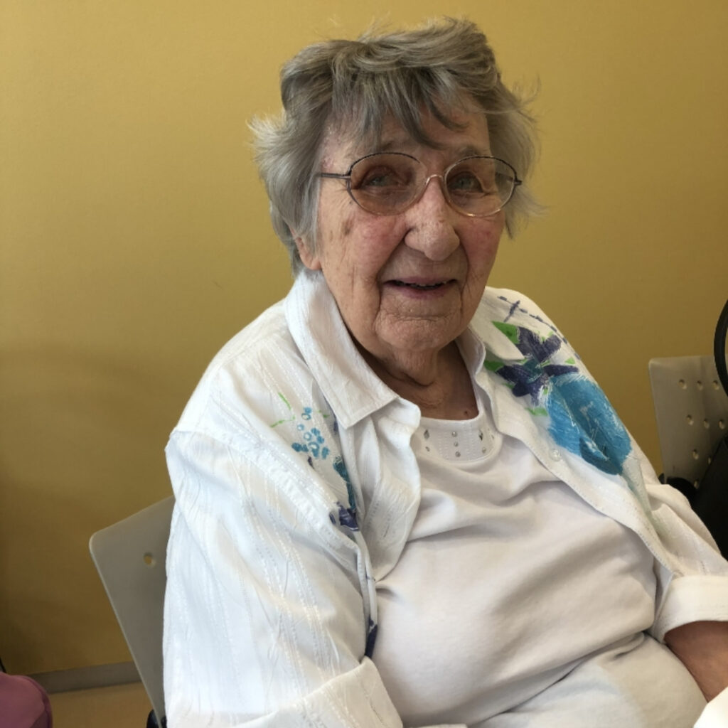 An elderly woman seated and smiling.