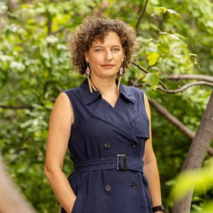 A woman wearing a navy outfit standing in front of some greenery
